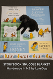 Storybook snuggle blanket with Winnie the Pooh designs and a black dog lying on it.